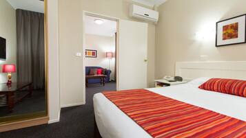 A hotel room with a large bed, a desk with a lamp, a chair, a small table, and a mirror.