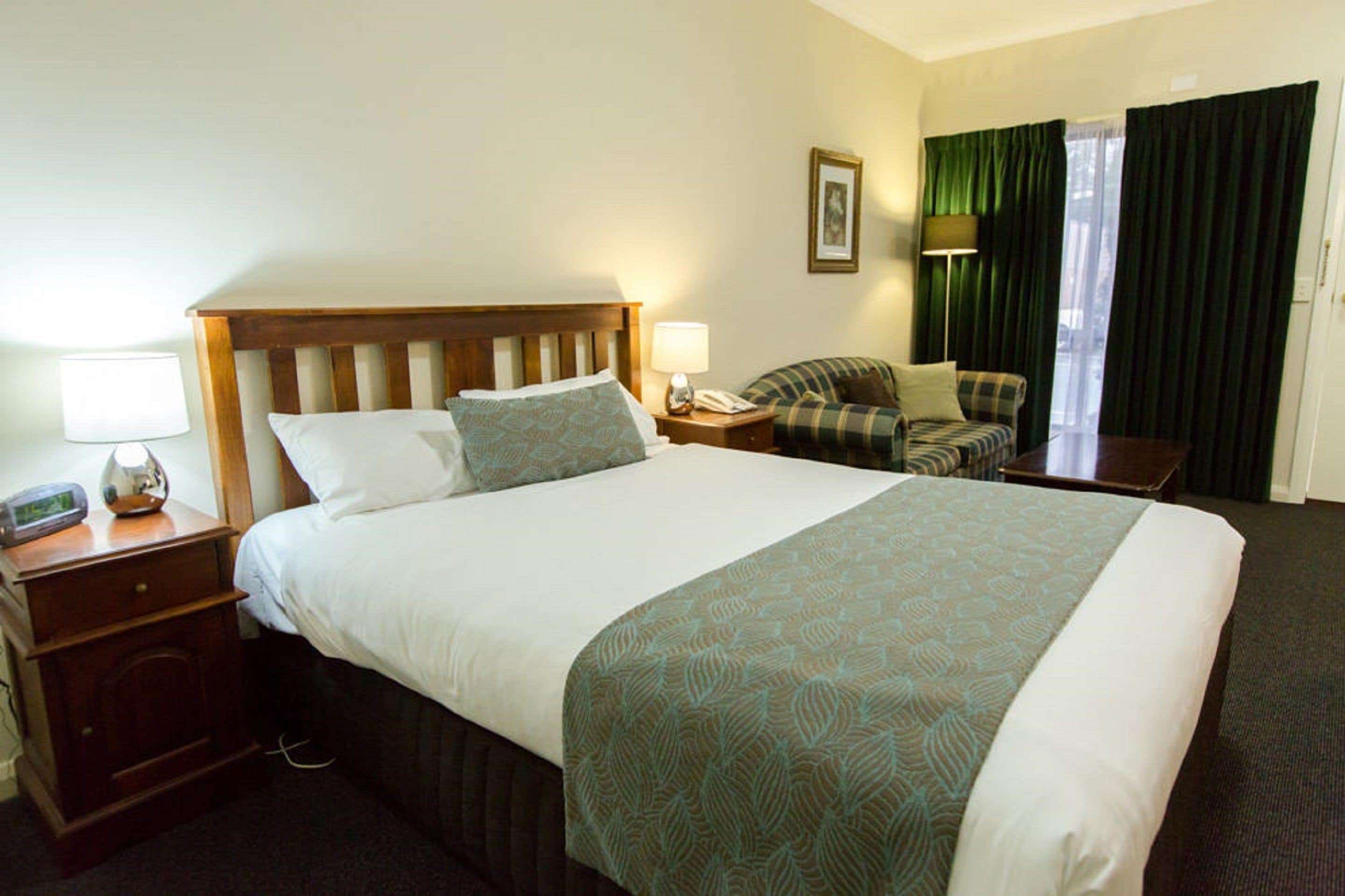 Una habitación de hotel con una cama grande, una mesita de noche con lámpara, una silla y un escritorio con lámpara.