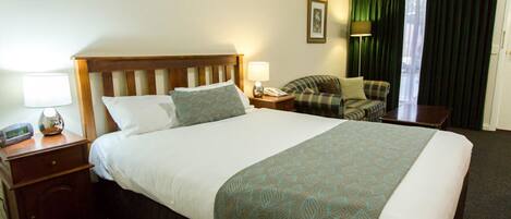 Una habitación de hotel con una cama grande, una mesita de noche con lámpara, una silla y un escritorio con lámpara.