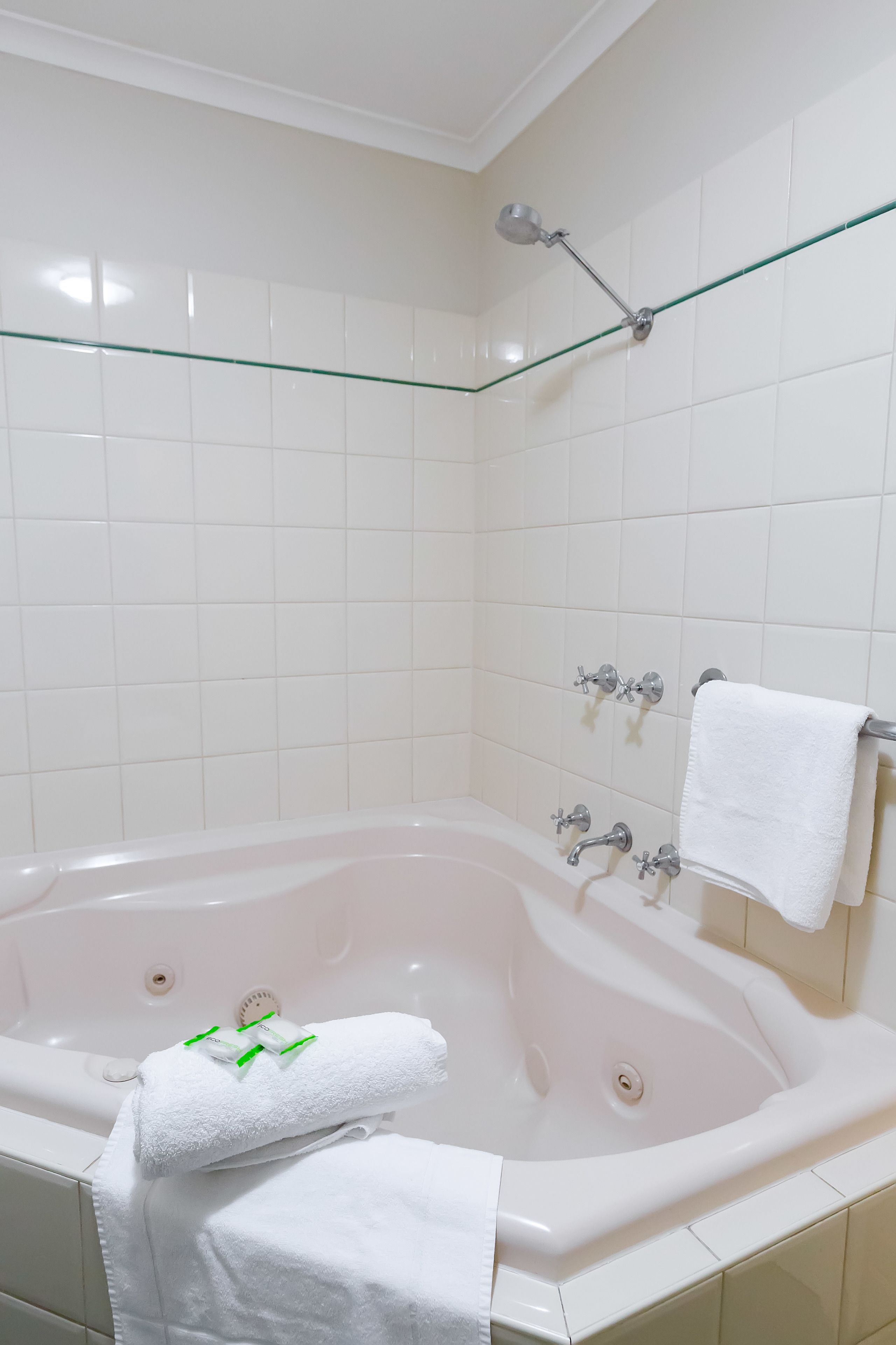 Una bañera blanca con un estante de vidrio, un perchero y un cabezal de ducha.