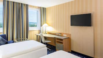 A hotel room with two beds, a desk, a chair, a TV, and a window with curtains.