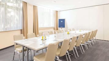 Et mødelokale med et langt bord, beige stole og en projektorskærm.