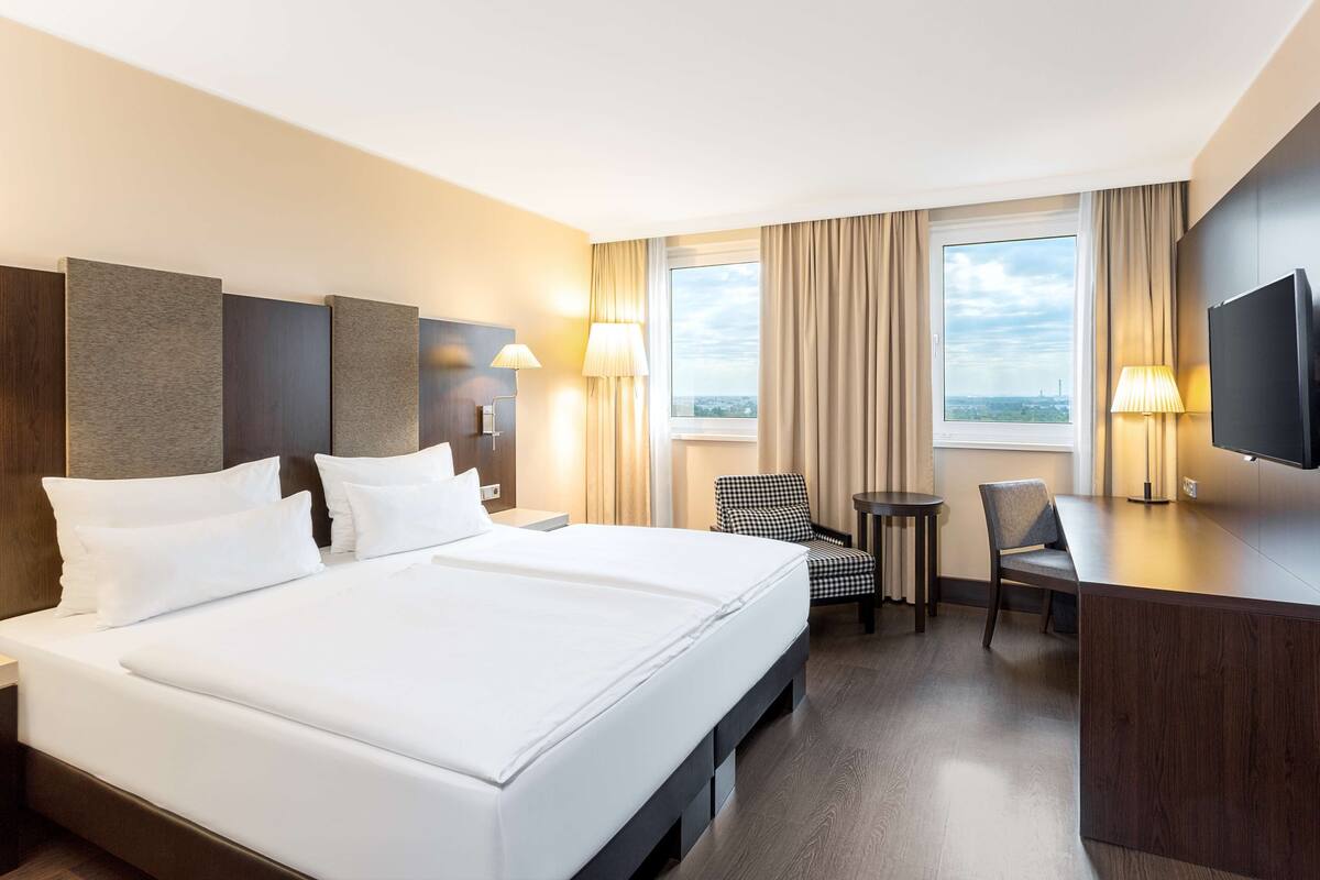 A hotel room with a large bed, a desk, a chair, a TV, and a window with curtains.