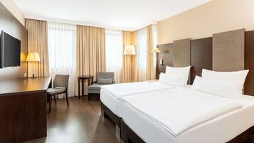 A hotel room with a large bed, a desk with a flat-screen TV, two lamps, a chair, and a small table.