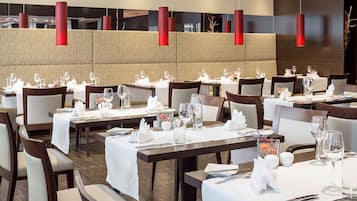 Un restaurante con varias mesas dispuestas para comer, con manteles blancos y cubiertos ordenados.