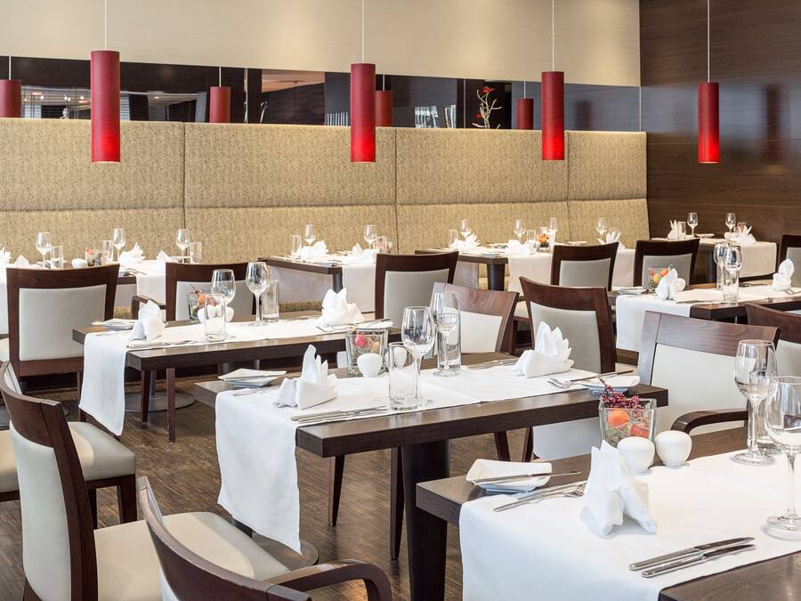 Un restaurante con varias mesas dispuestas para comer, con manteles blancos y cubiertos ordenados.