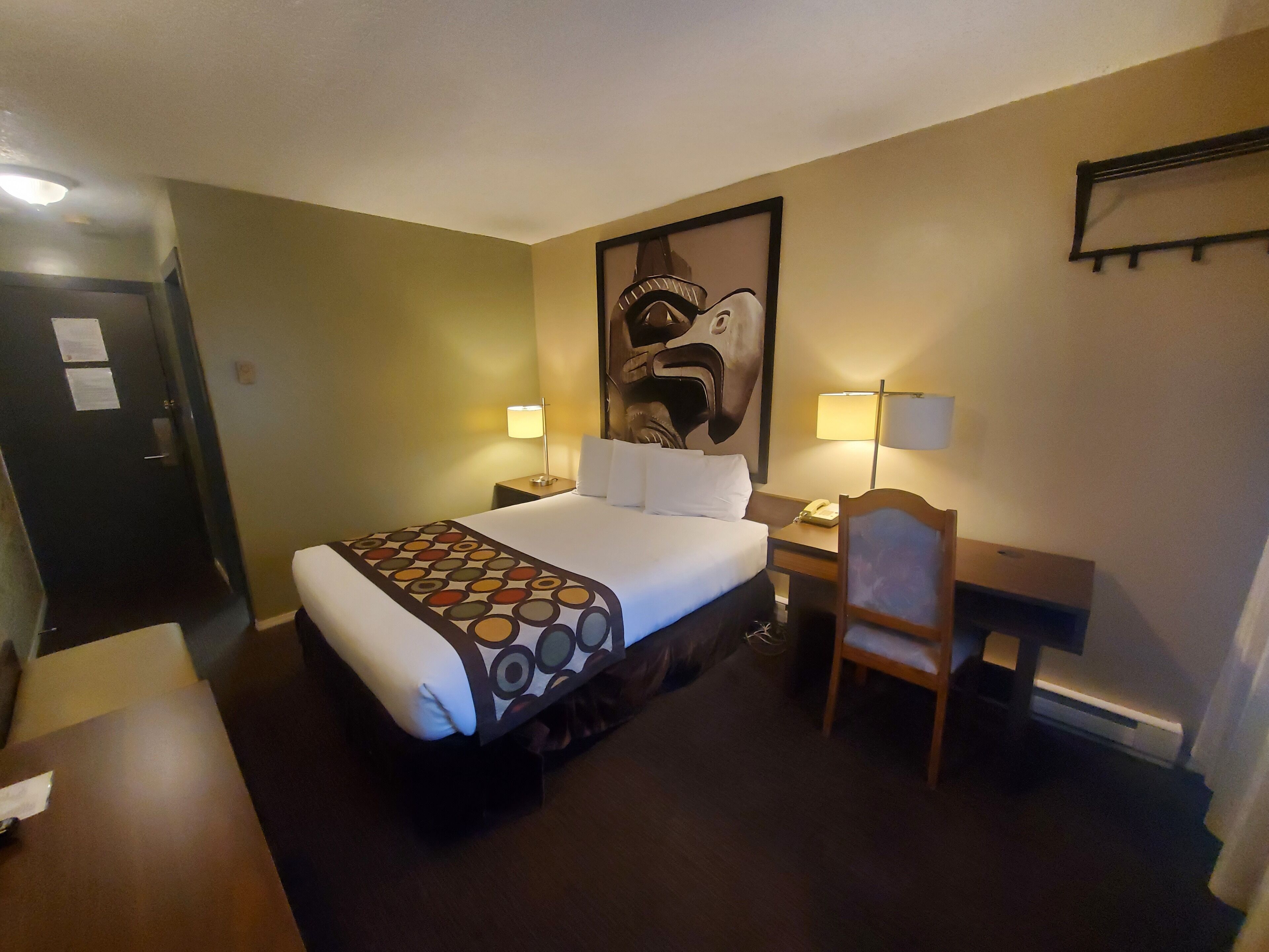 Habitación de hotel con cama, dos lámparas de noche, escritorio con silla y un cuadro abstracto grande en la pared.