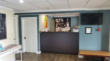 A reception area with a reception desk, a bench, a framed sign, a mounted television, and a door.