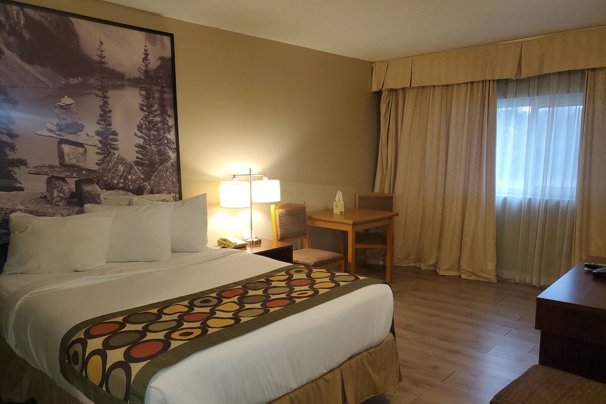 Una habitación de hotel con una cama grande, un escritorio, una silla, una lámpara y un cuadro en la pared.