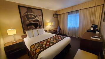 A hotel room with a large bed, two bedside tables, a desk, a chair, a large abstract painting on the wall, and a window with curtains.
