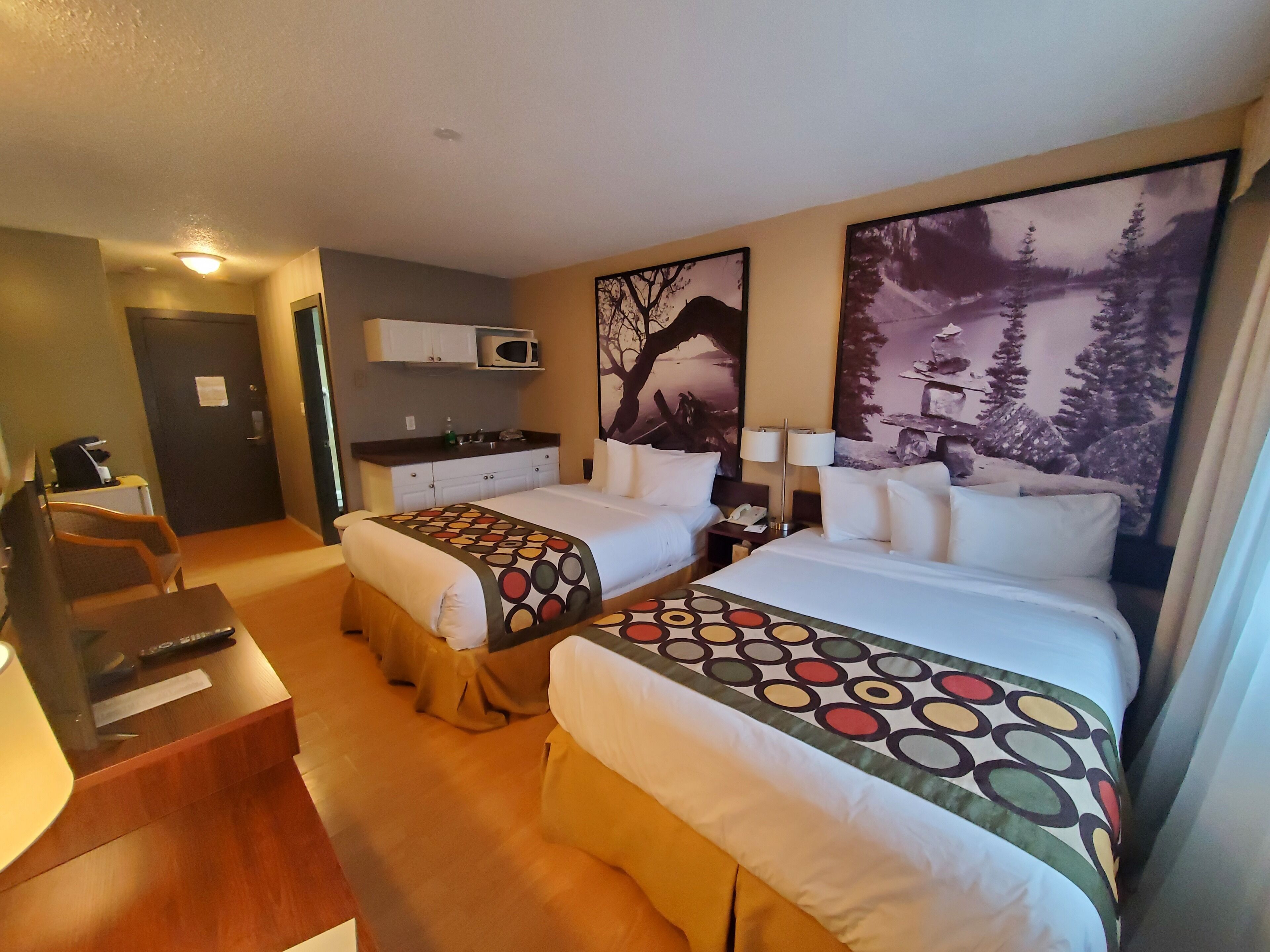 Une chambre d’hôtel avec deux lits, un bureau, une chaise, un four à micro-ondes et une petite kitchenette.