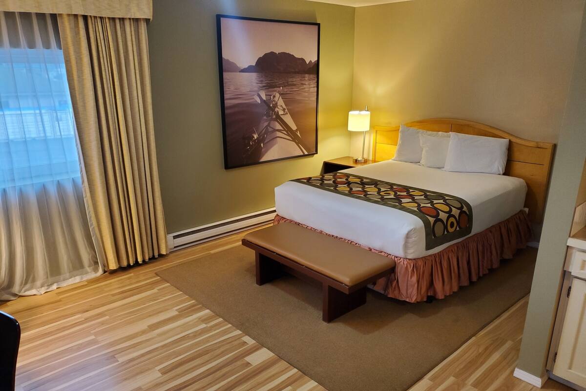 Habitación de hotel con cama, banca, lámpara y un cuadro de un bote en el agua.