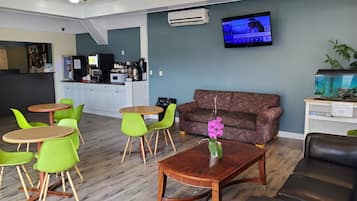 Una zona d'estar moderna amb cadires verdes, una taula de cafè de fusta, un sofà marró i una televisió penjada a la paret.