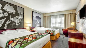 A hotel room with two beds, a desk, a chair, a TV, and large framed pictures on the walls.