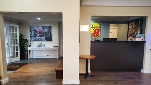 Un vestíbulo de hotel con una recepción, un banco, una mesita y un cartel grande de un autobús rojo en la pared.