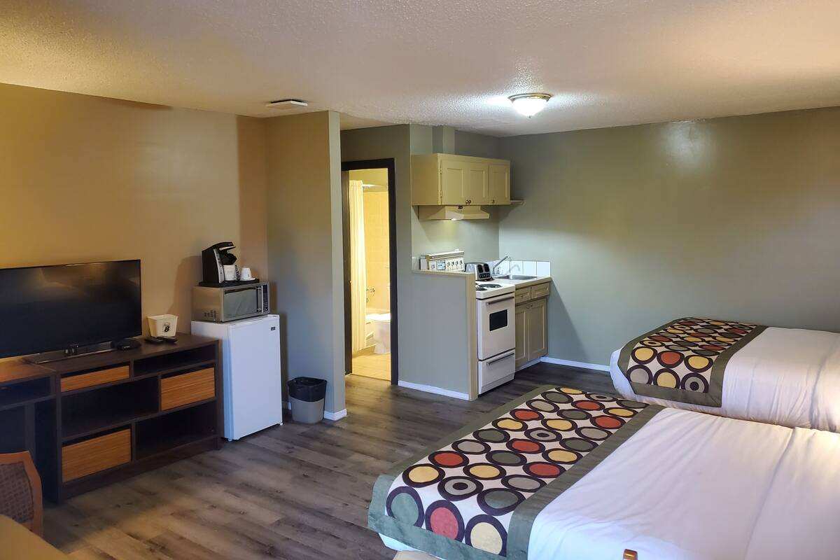 Habitación de hotel con televisión, una kitchenette pequeña, cama con ropa de cama estampada y suelo de madera.