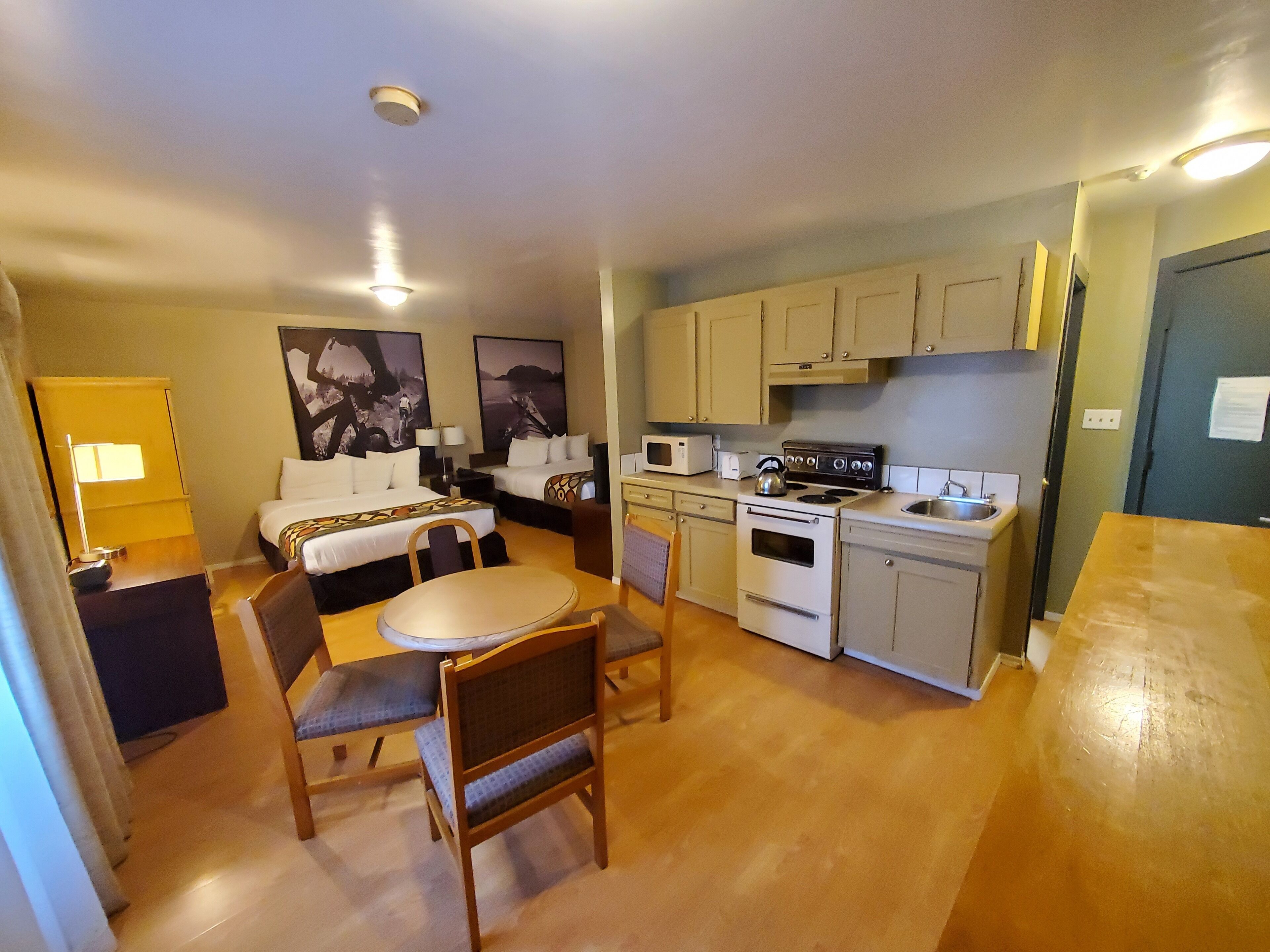 A compact hotel room with a kitchenette, a dining area, and a bed.