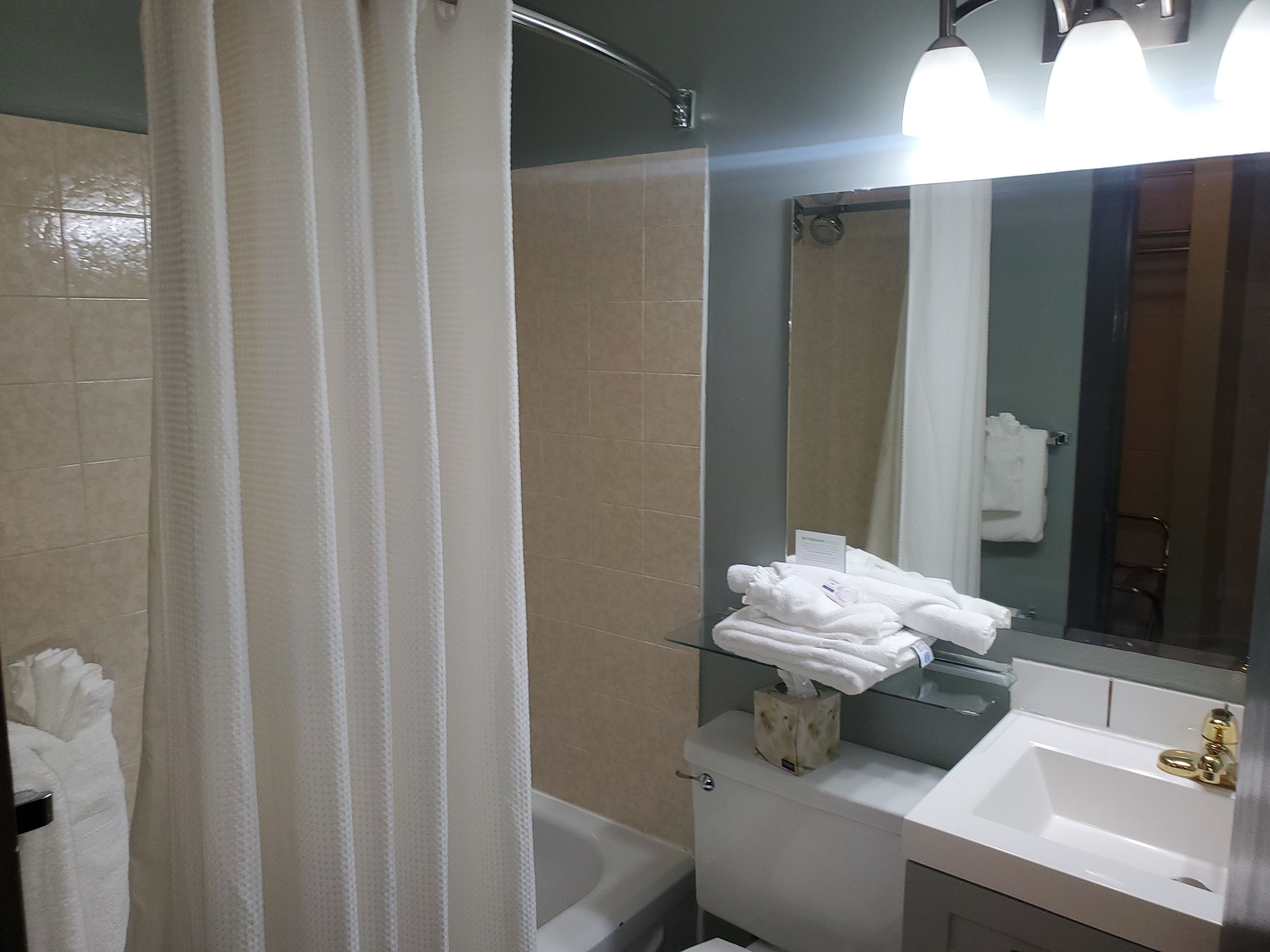 Baño con cabina de ducha de vidrio, inodoro, lavamanos con grifo dorado y espejo con toallero.