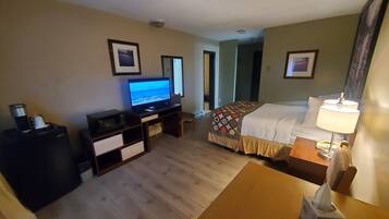 A hotel room with a bed, a desk, a television, a bedside table with a lamp, and a trash bin.