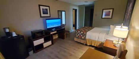 A hotel room with a bed, a desk, a television, a bedside table with a lamp, and a trash bin.