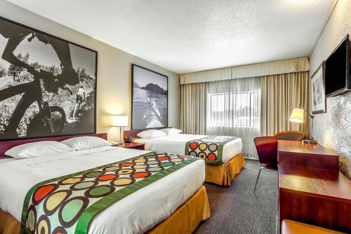 Habitación de hotel con dos camas, un escritorio, una silla, un televisor y obras de arte en las paredes.