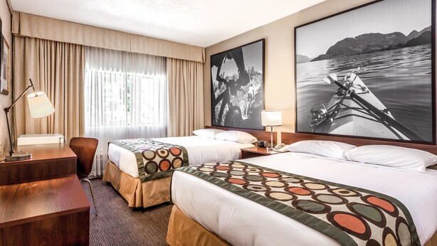 Habitación de hotel con dos camas, un escritorio, una silla, una lámpara y un cuadro grande con una imagen de un kayak en el agua.