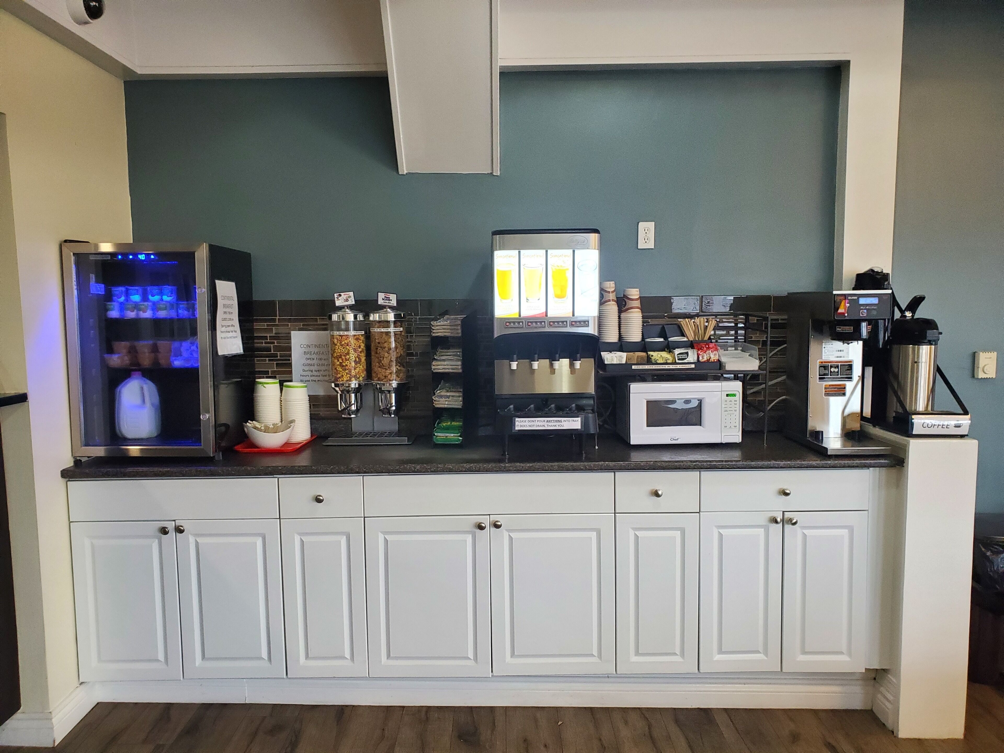 Een kitchenette met een koelkast, koffieapparaat, magnetron en etensdispensers.