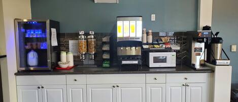 A kitchenette with a refrigerator, coffee machine, microwave, and food dispensers.