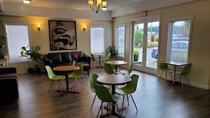 Una habitación amplia con piso de madera, sillas verdes, un sofá marrón y un candelabro.