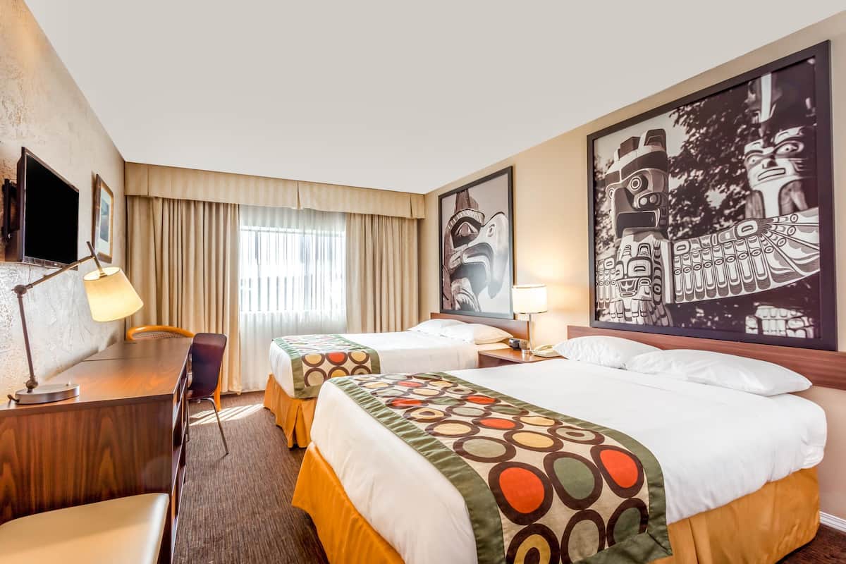 Habitación de hotel con dos camas, un escritorio, una silla, televisor y obras de arte en las paredes.