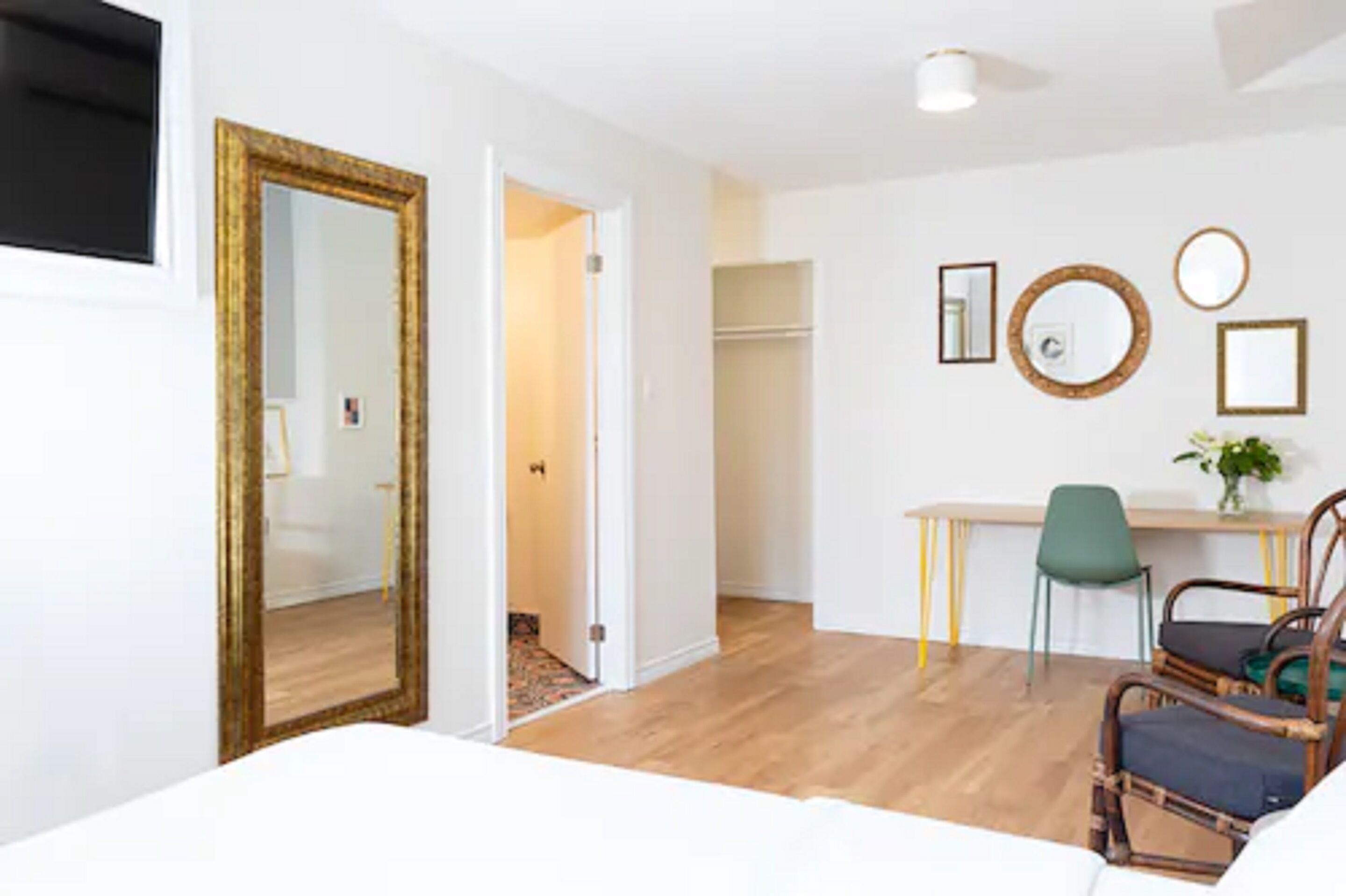 Una habitación de hotel con suelo de madera, una cama, un escritorio con silla, un espejo y un armario.