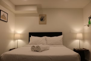 Een hotelkamer met een opgemaakt bed, twee bedlampen, een lijst met kunstwerk aan de muur, en een klein nachtkastje met een groene vaas.