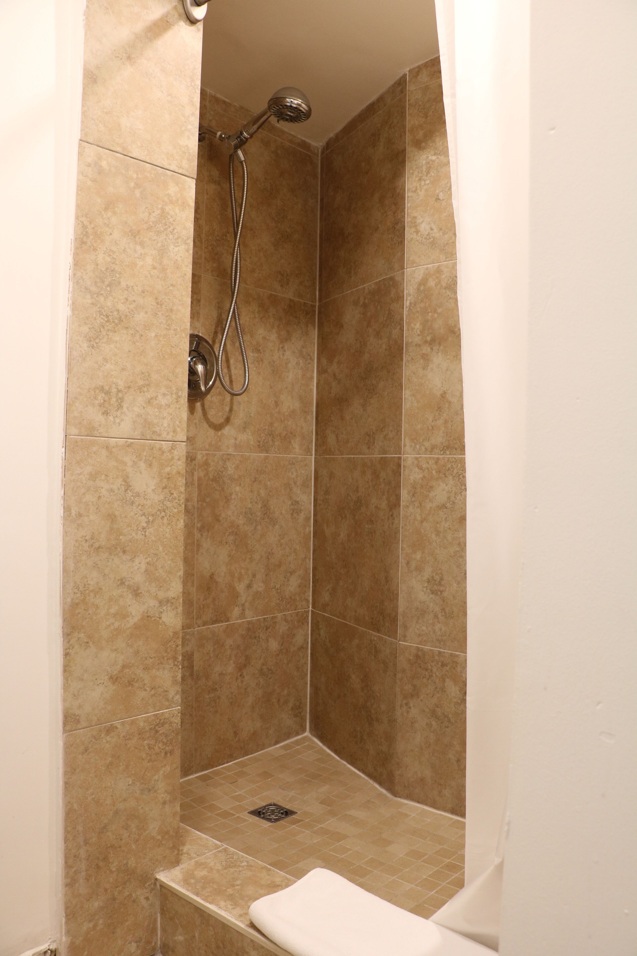 A small, enclosed shower area with beige tiles and a handheld showerhead.