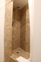 Een kleine, afgesloten douchecabine met beige tegels en een handdouche.