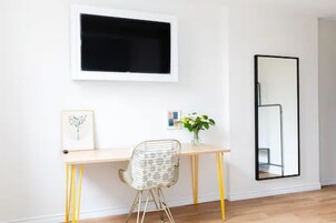 Een kamer met een bureau, stoel, ingelijst kunstwerk en een spiegel.