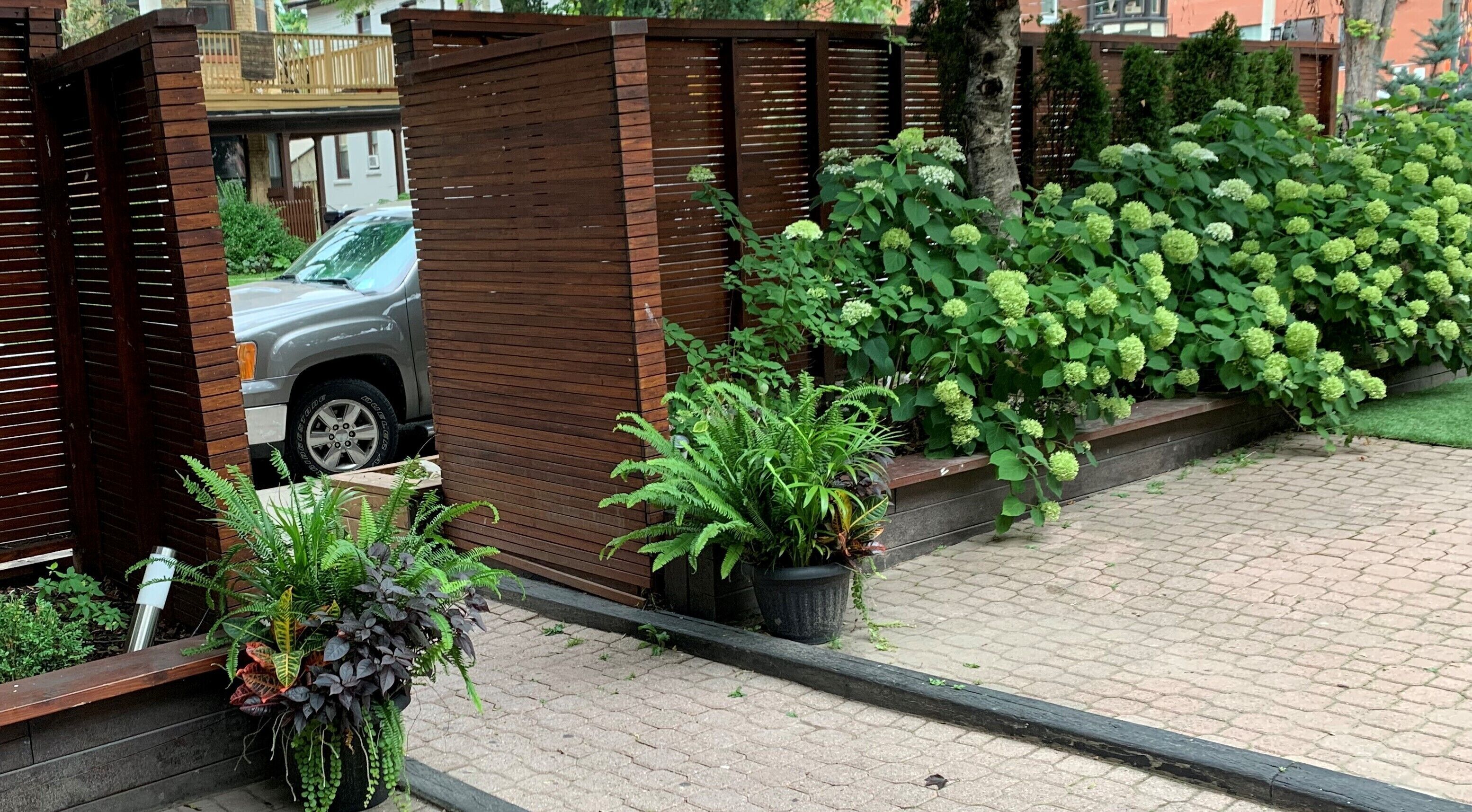 Ein begrenzter Eingangsbereich mit einem geparkten Auto, umgeben von üppiger Vegetation und einem Pflasterweg.