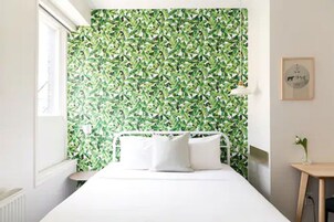 Een slaapkamer met groen bladeren behang, een wit bed en een klein nachtkastje met een lamp.