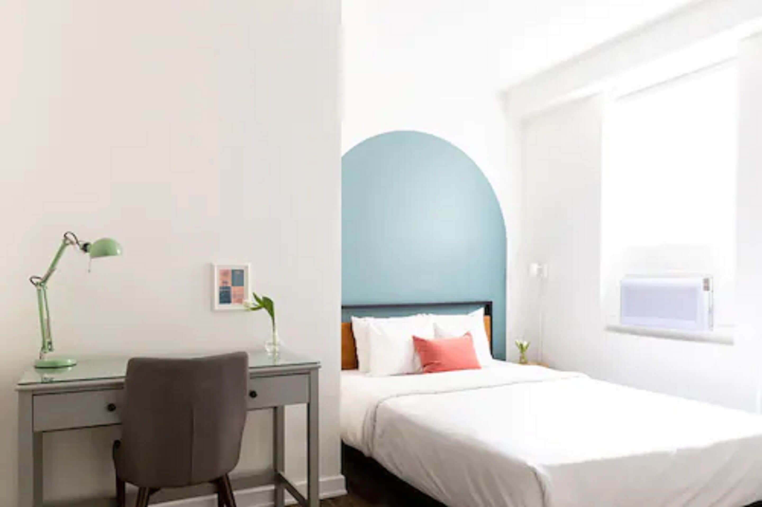 Un dormitorio con una cama, un escritorio, una silla, una ventana y una pared con un arco azul.
