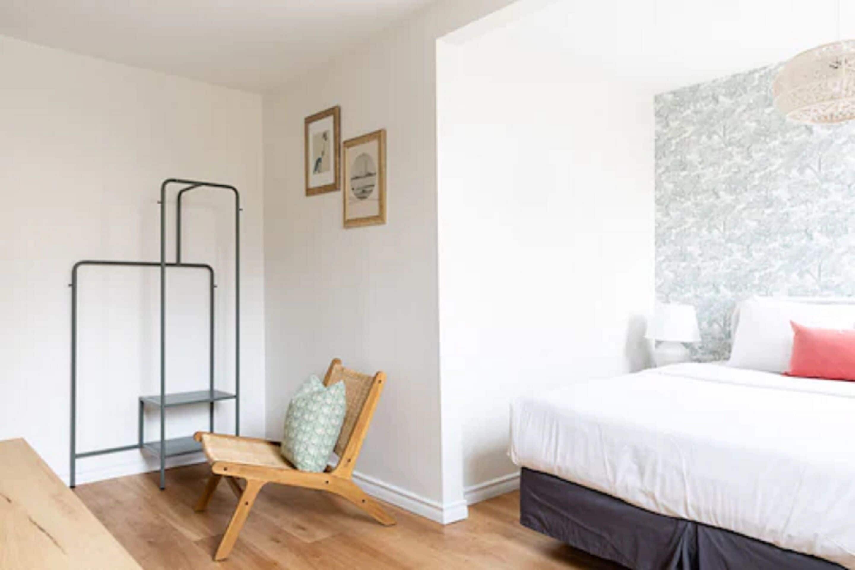 Un dormitorio con cama, una silla de madera, una estantería metálica y cuadros enmarcados en la pared.