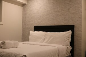 Een netjes opgemaakt bed met witte lakens en kussens, een zwart hoofdeinde en een gestructureerde wand erachter.