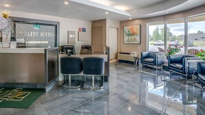 A hotel reception area with a reception desk, two black bar stools, a large window with a view of the parking lot, and a painting on the wall. - Quality Suites (Ste Anne de Beaupre)