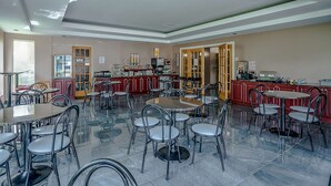 A spacious dining area with multiple tables and chairs, a kitchen area with appliances, and a view through a glass door. - Quality Suites (Ste Anne de Beaupre)