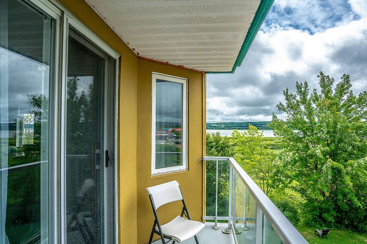A balcony with a white chair, a glass door, and a view of greenery and a lake.