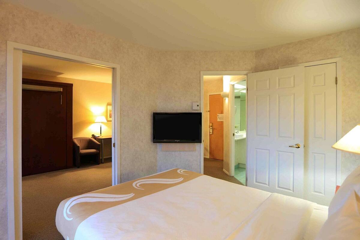 A hotel room with a bed, a television, a door, and a bathroom visible through an open door.