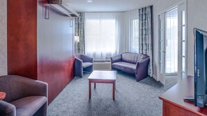 A modern hotel room with a large window, two sofas, a small table, and a television. - Quality Suites (Ste Anne de Beaupre)