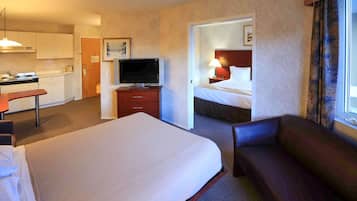 A hotel room with a bed, a sofa, a TV, a desk, and a kitchenette.