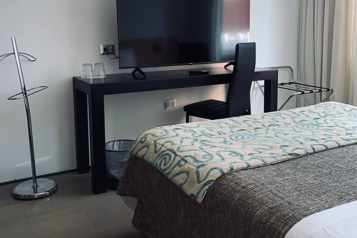Una habitación de hotel con cama, escritorio con televisor, silla y lámpara de pie.