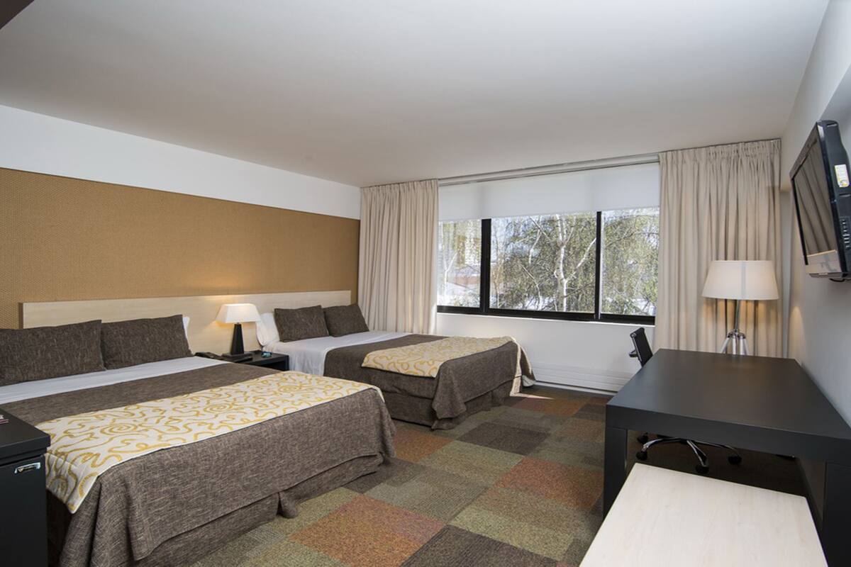 Habitación de hotel con dos camas, un escritorio, un televisor y una ventana con cortinas.