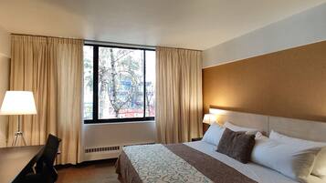 Una camera d'albergo con un letto, una scrivania, una sedia e una finestra con tende.