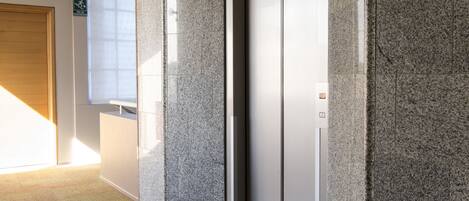 Un ascenseur moderne dans un couloir aux murs en granit et au tapis à motifs.